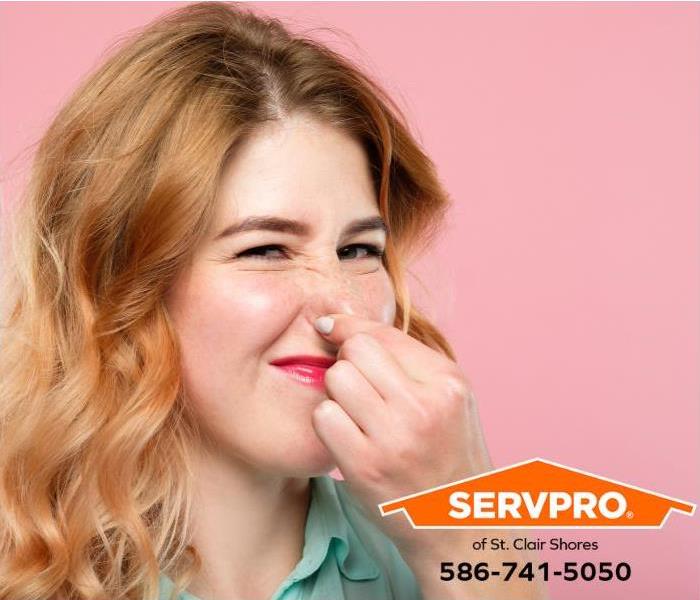 A woman holds her nose to avoid smelling a bad odor.