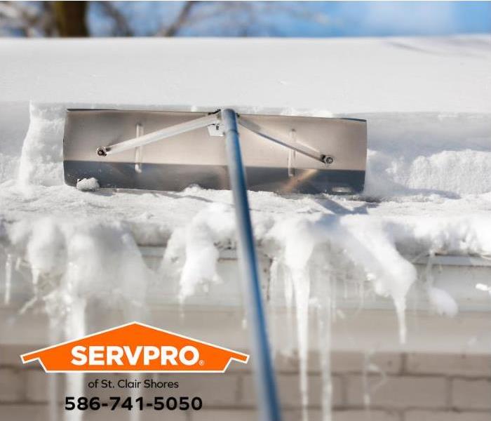 A person uses a snow rake to clear snow and ice dams from a roof.