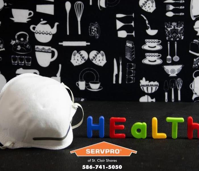 A white facemask rests in front of a poster showing household and kitchen items.