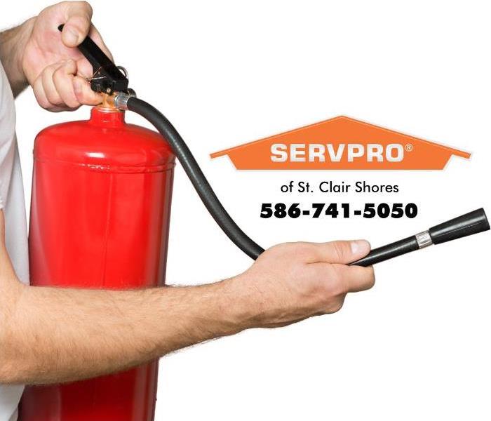 A man is holding a fire extinguisher and pointing the hose in demonstration of its use. 